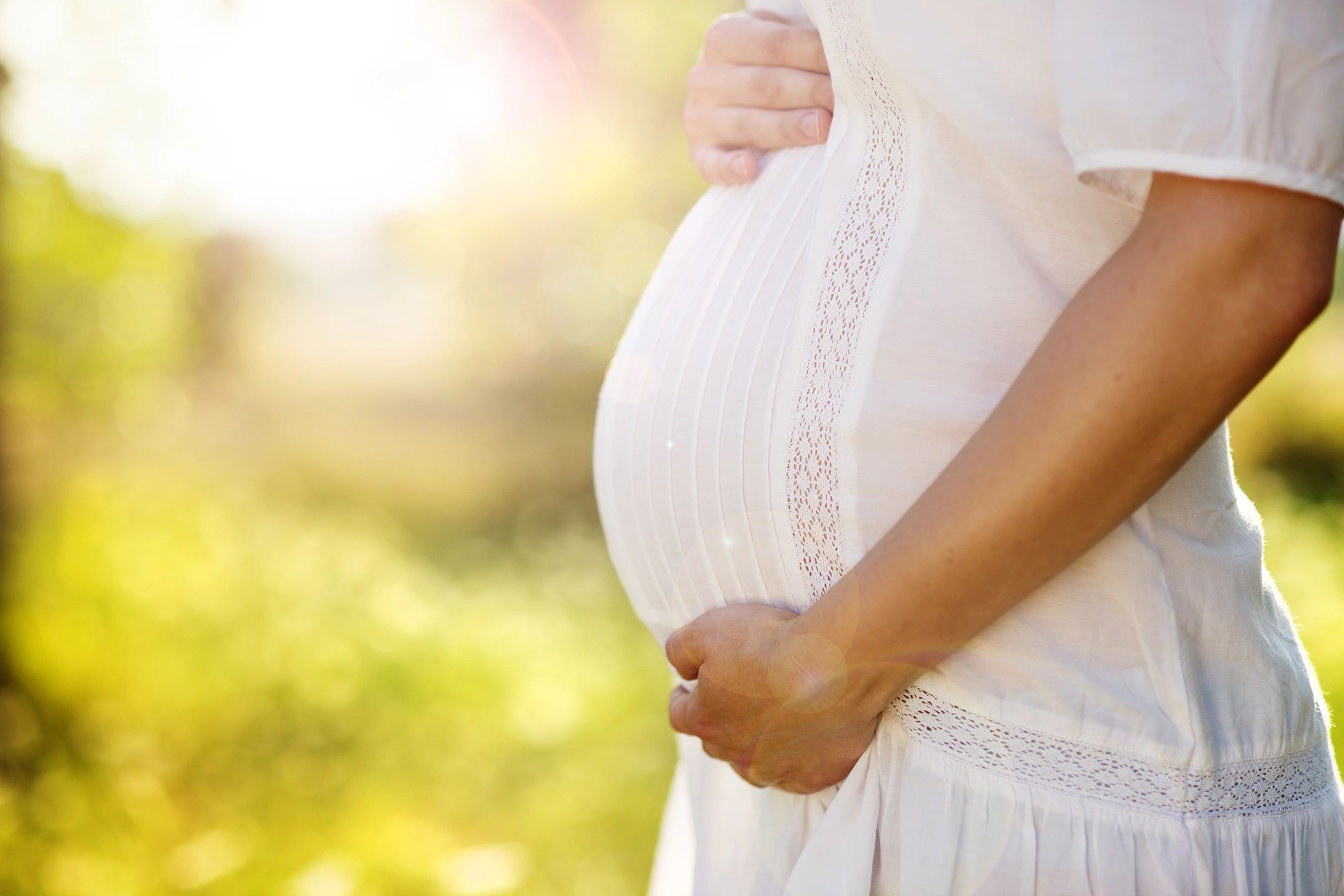 Pregnant woman stands in sunshine holding her belly