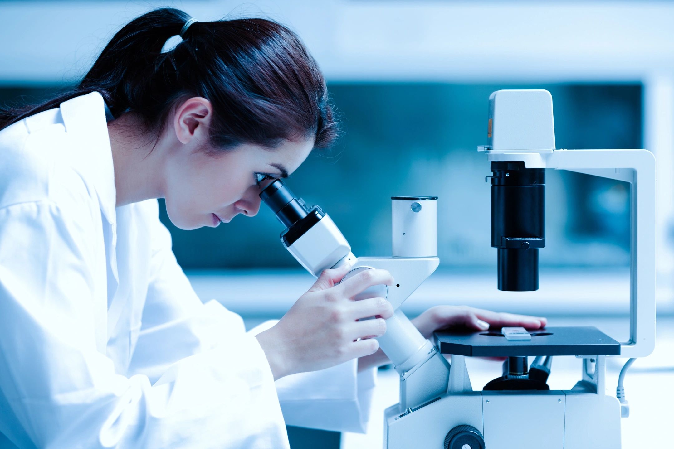 woman in lab coat looking through microscope