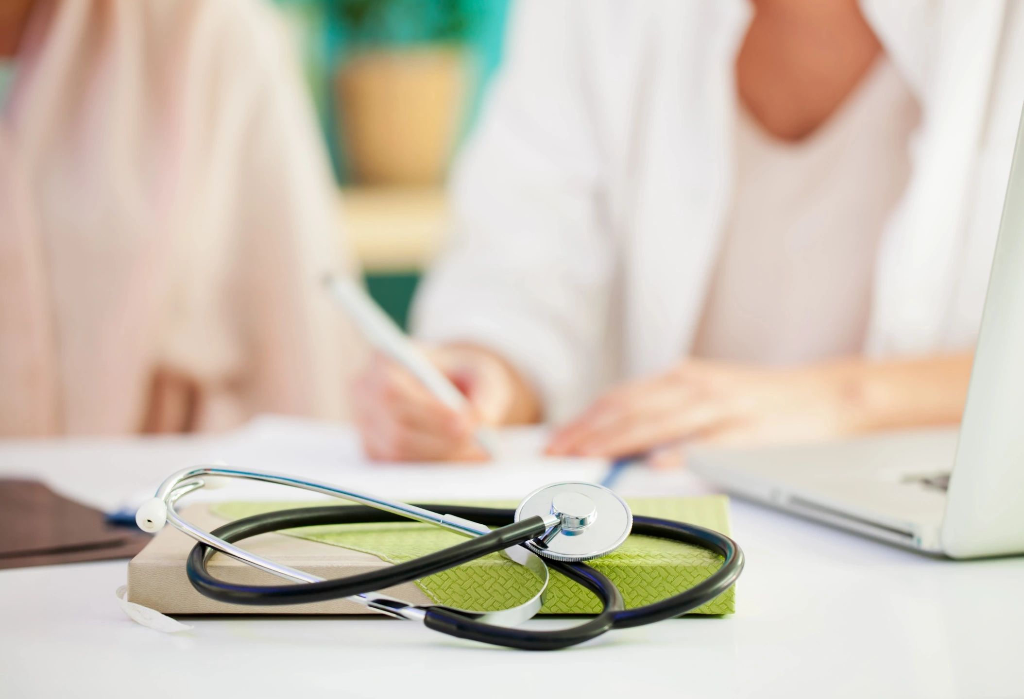 blurry doctor and patient in background with stethoscope on a notebook